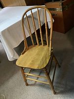 Photo of an old solid wooden chair with rounded spindle backrest and turned legs, showing the light wood finish and overall condition.