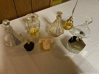 Eight assorted vintage crystal perfume bottles displayed on white surface, various shapes and stoppers visible.