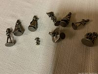 Photo showing 9 small pewter Disney character figurines arranged on cloth, viewed from above, detailing bases downwards.