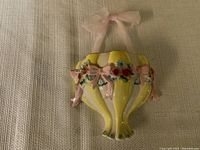 Front view of the yellow ceramic pocket vase showing pink bows, floral decorations, and pink sheer ribbon bow.