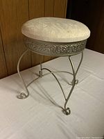 Vanity stool angled side view showing silver metal scrollwork legs and padded round seat.