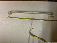 Full view of vintage glass towel bar lying flat with tape measure running alongside showing length about 24 inches.