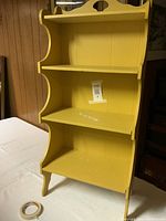 Three-quarter front view of yellow wooden shelf showing shape and shelves