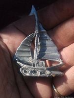 Pewter sail ship ornament held in hand showing front texture and waves base