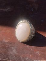 Close-up front view of gold tone adjustable ring with large oval rose quartz stone showing smooth polished stone and detailed bezel and band.