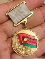 Front side of the round medal showing colorful enamel flags and laurel with sunburst design.