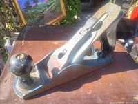 Side angle showing metal body, black wooden front and rear handles, exposed blade, and rust on the sole of the plane.