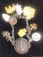 Photo showing various carved ivory-like charms, silver military medal charms, and vintage coins on the bracelet, set against a black background.