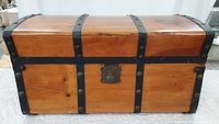 Front view of curved dome top wood Jenny Lind trunk with black metal banding and brass lock plate.