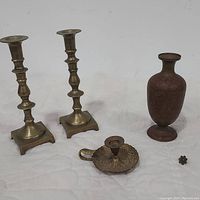 Full view of all four items arranged together showing two tall brass candlesticks, a bronze gilded vase, Damascus brass chamberstick with leaf thumb rest and finger loop, and a small decorative brass piece