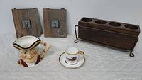 Photo of all items including wooden plaques, sugar mold in iron caddy, character jug, and china cup with saucer.