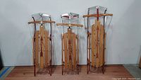 Three vintage Flexible Flyer sleds standing upright showing wood slats, metal runners, and steering bars with pull ropes.
