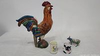 All four items arranged side by side: rooster, Deruta mug, Wang’s cow mug, CowParade figurine