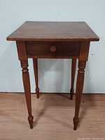 Front view showing the cherry wood one drawer stand with tapered legs and round knob on drawer.