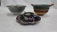 Blue-gray stoneware bowl, purple-white glazed cup and dish, and woven basket bowl with blue handles and rim.