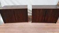 Two dark wood rectangular cabinets side by side showing front view with doors closed, revealing wood grain pattern and integrated vertical handles.