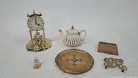 Overview of all items: Elgin quartz pendulum clock (missing dome), mini dome clock, John Sadler English teapot with gold swirl, hand-painted serving tray, brass trivet, and small plaque.