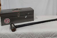 Metal toolbox and Village Blacksmith sledgehammer on white surface.