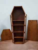 Front view of coffin-shaped wooden shelving with lid and side panels removed showing shelves.