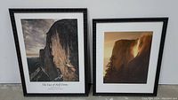 Photo showing two large framed landscape photos side by side on a floor against a white wall. The left is titled 'The Face of Half Dome' and the right is a sunset Yosemite print signed by the artist.
