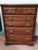 Front view of the vintage Bassett chest of drawers, showing five drawers with brass handles and carved wood detailing.