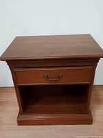 Front view of Ethan Allen nightstand showing drawer with brass handle and open lower shelf, wood grain and finish visible