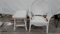 White wicker chair and side table set displayed on a concrete floor against a white backdrop, showing the full view of both items with some peeling paint visible.