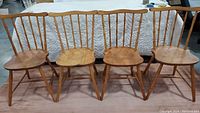 Four vintage wooden spindle back dining chairs arranged side by side showing full front view.