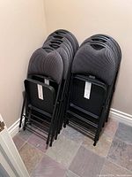Two stacks of six chairs each leaning against a wall on slate tile flooring
