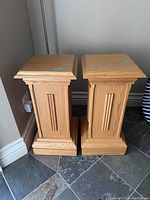 Two light oak wood pedestal stands on tiled floor near wall