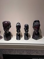 Front view of four wood carved African sculptures showing detailed facial features and hairstyles.