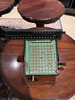 Top view of antique Monroe calculating machine showing green metal body, numeric keys arranged in a grid, and numeric display sliders on the top bar.