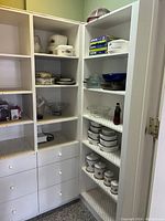 Wide view of pantry shelves showing assortment of ceramic, glass, and metal kitchenware including Corning Ware and Borosil items