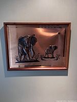 Frontal view of copper artwork showing large and small elephant figures in relief, framed in wood.
