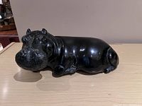 Front view of black stone hippo sculpture on light wood surface against neutral background