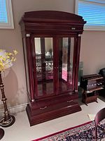 Front view of the large wooden display cabinet with glass doors and drawer below, showing its polished dark wood finish and crown molding top.