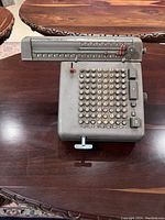 Top-down view of Monroe LA 7-160 calculating machine placed on a wooden table, shows keypad, numeric display, and crank handle.