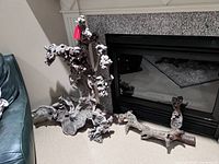 Wide view of two original Mombasa driftwood pieces near a fireplace on carpeted floor, showing both large and smaller pieces' shapes and textures.