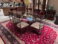 Oval glass dining table with metal base and six metal chairs with striped cushions arranged on a red patterned rug.