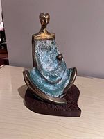 Front and angled view of signed bronze sculpture on wood base showing patina and abstract human figure shape.