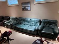 Wide view of vintage green leather sofa with two matching armchairs in room setting.