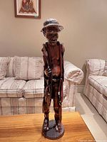 Front view of the wooden fisherman sculpture on a wooden table with sofas in the background.