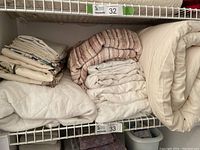 Bedding items folded on white wire shelving: mattress pad, duvet, sheets, and throw blanket.