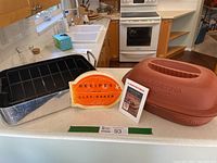Overview photo of entire lot showing ceramic clay baker base, lid, and two recipe booklets.