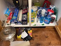 Wider view of cabinet and floor showing full assortment of kitchen cleaners, food wrap boxes, compost bucket and trash bags.