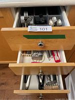 Three kitchen drawers partially opened showing various cutlery and kitchen utensils organized in plastic trays.