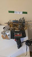 Photo showing Craftsman corded electric drill next to wooden drill bit holders filled with assorted drill bits