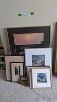 Group photo of assorted framed pictures including a large orange sunset, mountain and coastal scenes, and smaller prints and paintings.
