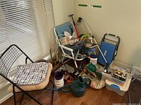 Wide view of lot showing chairs, gardening tools, watering cans, containers and BBQ accessories in corner of room.