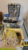 Photo of the hardware lot showing a tall organizer box with multiple small drawers, a clear plastic bin with assorted tools and supplies, and a yellow box containing coiled rope and other hardware items.